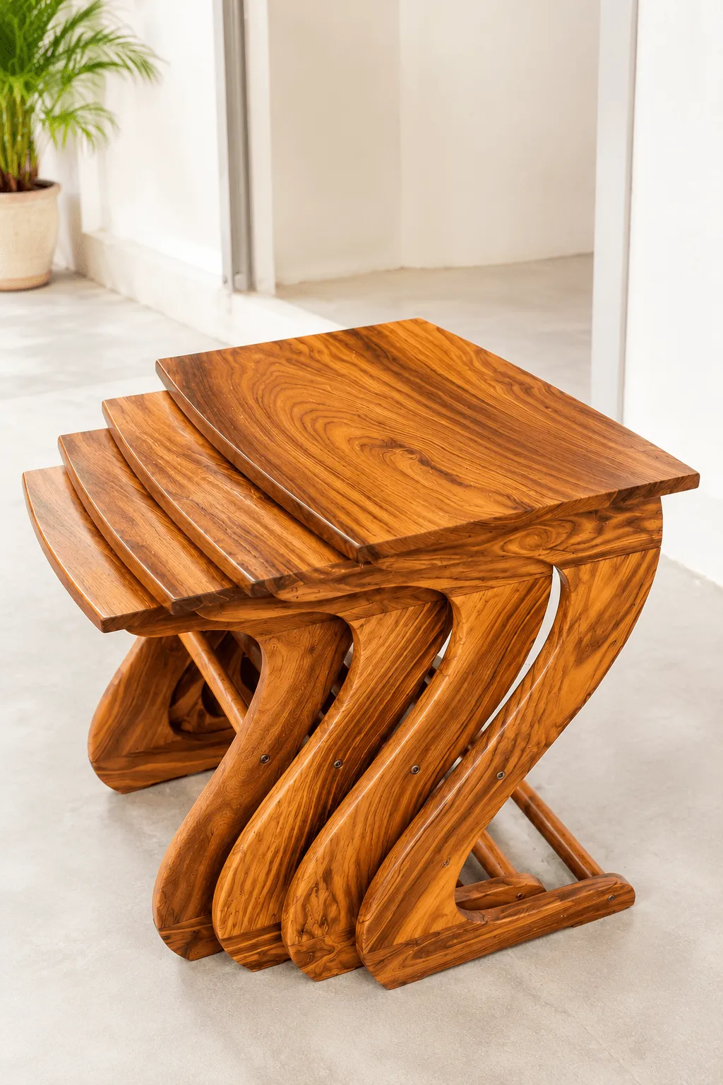 A set of three nested wooden tables with a distinctive Z-shaped base, standing on a light concrete floor in a bright, minimalist room.